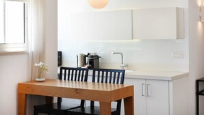 A modern kitchen with white cabinetry, a wooden dining table, and a hanging light fixture. - Hilton Area 2BR by HolyGuest (Tel Aviv-Yafo)