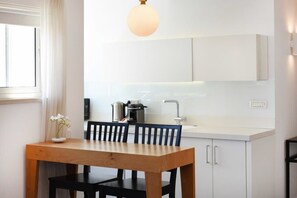 A modern kitchen with white cabinetry, a wooden dining table, and a hanging light fixture. - Hilton Area 2BR by HolyGuest (Tel Aviv-Yafo)
