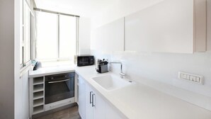 A modern kitchen with white cabinetry, a built-in oven, a microwave, and a sink. - Hilton Area 2BR by HolyGuest (Tel Aviv-Yafo)