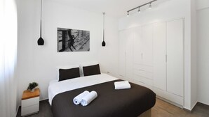 A modern hotel room with a large bed, a wardrobe, a nightstand, and a wall-mounted picture. - Hilton Area 2BR by HolyGuest (Tel Aviv-Yafo)