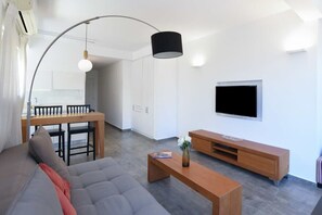 A modern living room with a sofa, coffee table, and TV. There is a dining area with a table and chairs. - Hilton Area 2BR by HolyGuest (Tel Aviv-Yafo)