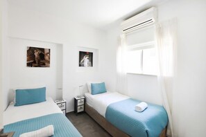 A hotel room with two beds, a window with curtains, and a wall-mounted air conditioner. - Hilton Area 2BR by HolyGuest (Tel Aviv-Yafo)