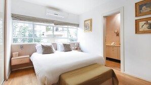Een slaapkamer met een groot bed, een raam met uitzicht, een nachtkastje en een klein bankje.