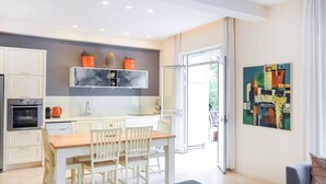 Een moderne keuken met witte kasten, een marmeren spatwand, en een eethoek met een houten tafel en witte stoelen.