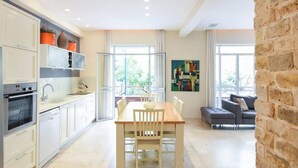 Een moderne keuken met witte kasten, een eethoek met een houten tafel en stoelen, en een zithoek met een bank en een schilderij aan de muur.