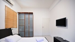 Habitació d'hotel moderna amb llit, televisió penjada a la paret, armari amb portes de vidre mat i una porta amb tirador.