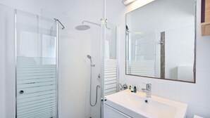 Un bany modern amb una dutxa de vidre, un mirall gran i un lavabo blanc.