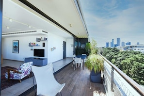 A balcony with a city view, a dining area with chairs and a table, and a TV on the wall.