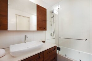 A bathroom with a white sink, wooden vanity, and a glass shower enclosure. - Spacious 2BR With Terrace in Rothschild by HolyGuest (Tel Aviv-Yafo)