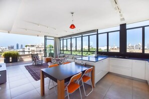 A modern kitchen with large windows, a dining area with orange chairs, and a city view.