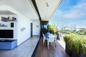 A modern living room with a flat-screen TV, bookshelves, and a dining area with a table and chairs.