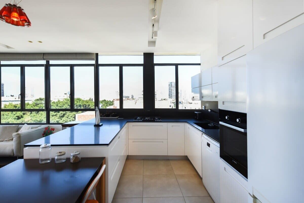A modern kitchen with white cabinets, a black countertop, and a view of the city through large windows.