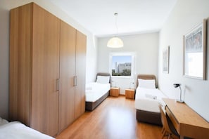 A modern bedroom with a large wardrobe, two beds, a desk, and a window with a view. - Red by HolyGuest (Tel Aviv)
