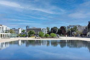 A public square with a reflective water feature, modern buildings, and a clear blue sky. - Red by HolyGuest (Tel Aviv)