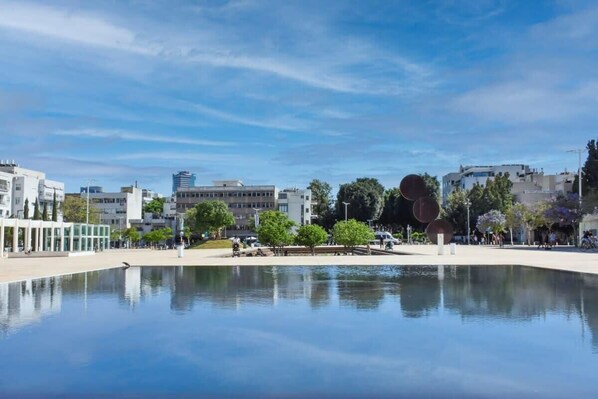 Una plaza pública con una fuente de agua reflectante, edificios modernos y árboles.