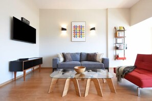 A modern living room with a sofa, a glass coffee table, a TV, and a bookshelf.