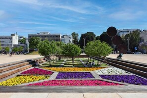 A public square with a central garden featuring colorful flower beds and a wooden bench area.