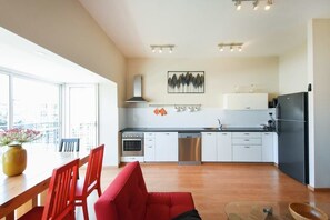 A modern kitchen with white cabinets, stainless steel appliances, and a black refrigerator. There is a dining area with a wooden table and red chairs.