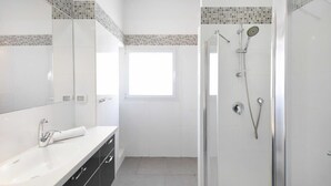 Une salle de bain avec une douche, un lavabo, un miroir et une fenêtre.