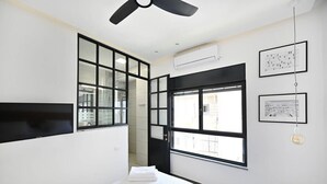 Ein modernes Hotelzimmer mit einem großen Bett, einem Deckenventilator, einem Fenster mit Blick und gerahmten Bildern an der Wand.