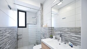 Ein modernes Badezimmer mit einem großen Spiegel, einem weißen Waschbecken und einer Duschkabine.