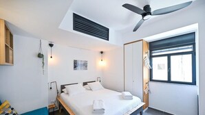 Ein modernes Schlafzimmer mit Bett, Nachttisch, Wandleuchte, Deckenventilator und einem Fenster mit Jalousien.