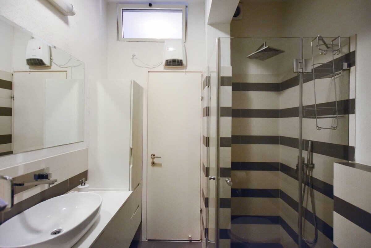 A bathroom with a white sink, a mirror, a shower with a glass door, and striped wall tiles.
