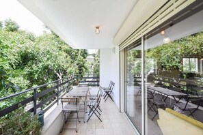 Een balkon met buitenmeubilair, glazen deuren en uitzicht op groen.