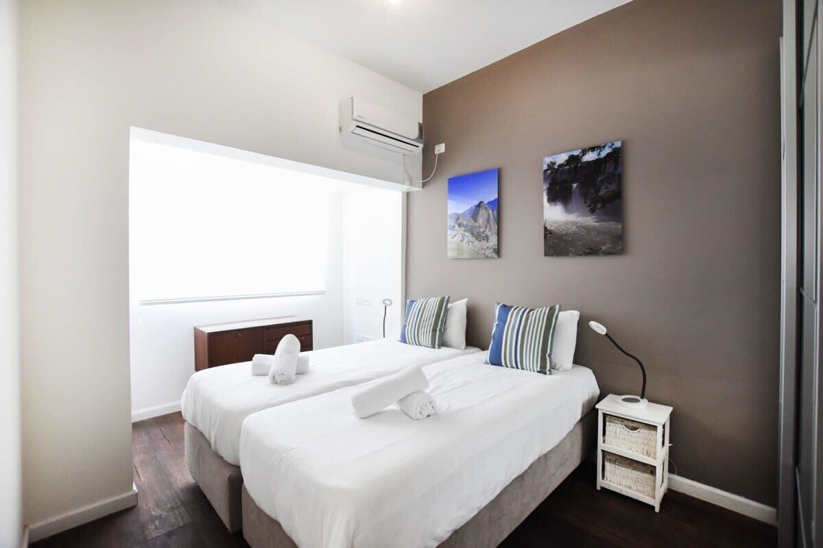 Ein Hotelzimmer mit zwei Betten, einem Nachttisch, einer Lampe und einer Wand-Klimaanlage.