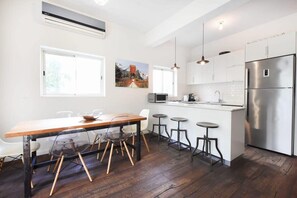 Une cuisine moderne avec une table à manger en bois, des tabourets de bar, un réfrigérateur en acier inoxydable et une grande fenêtre.