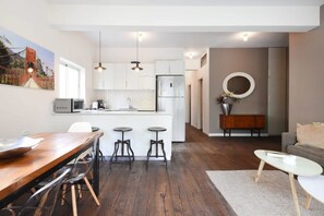 Une cuisine moderne avec des meubles blancs, un réfrigérateur en acier inoxydable et un coin repas comprenant une table en bois et des tabourets.