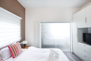 Une chambre d’hôtel équipée d’un lit, d’une télévision, d’une porte coulissante et d’une fenêtre avec des stores.