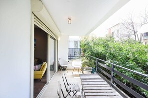Un balcon doté d’une terrasse en bois, d’une balustrade et offrant une vue sur la verdure et les bâtiments.