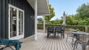 Une terrasse en bois avec des meubles d’extérieur, notamment une table et des chaises, ainsi qu’un espace salon abrité.