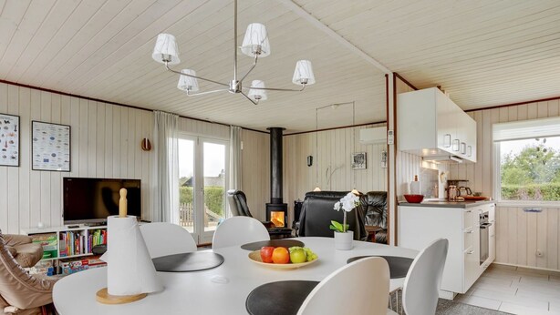 Une cuisine moderne dotée d’une cuisinière intégrée, un coin repas avec une table et des chaises blanches, et un téléviseur dans le salon.