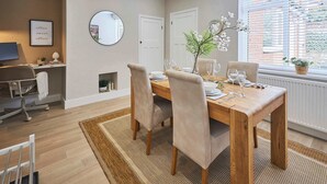 Un coin repas avec une table en bois dressée pour quatre personnes, entourée de chaises, d’un miroir rond et d’un panneau encadré accroché au mur.