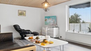 Un salón moderno con una mesa blanca, sillas de cuero negro, techo de madera y un ventanal con vistas al exterior.