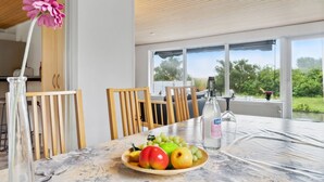 Un comedor con una mesa preparada para dos personas, con mantel floral, un plato de fruta y una botella de agua.