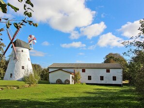 Un moulin à vent traditionnel et un bâtiment blanc doté d’un toit à pignon, entourés d’un champ verdoyant.