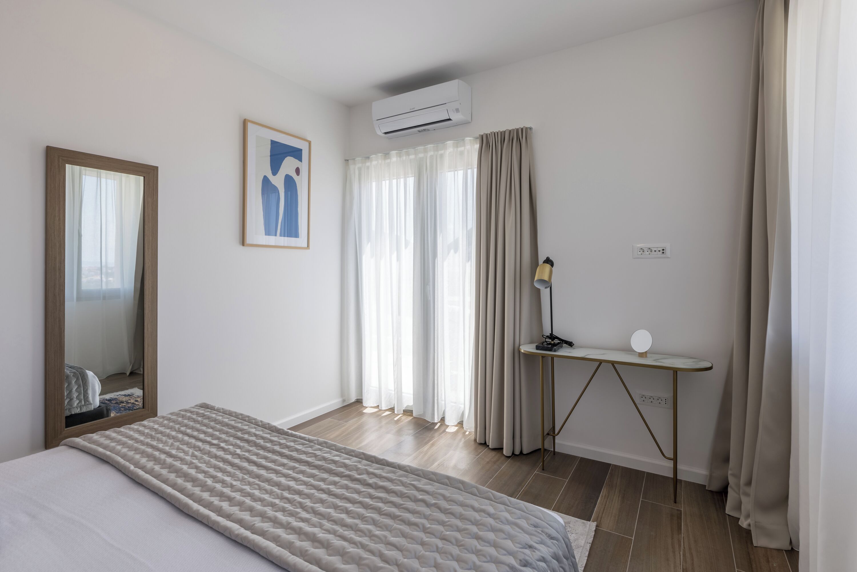 Quarto com cama, escrivaninha com luminária, espelho e ar-condicionado.