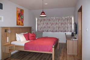 A bedroom with a wooden bed, a desk, a chair, a television, and a painting on the wall. - Tündérkert Panzió Őrség (Viszák)