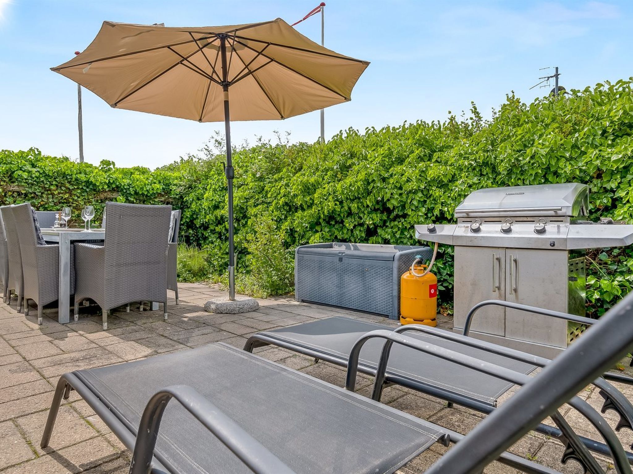 Une terrasse extérieure avec une table et des chaises, un barbecue et une bouteille de gaz.