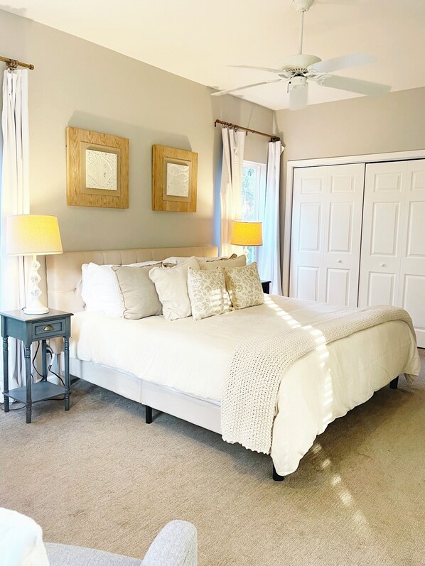 A neatly arranged bedroom with a bed, bedside lamps, a ceiling fan, and two framed pictures on the wall.