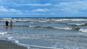 Ein Strand mit Wellen und einem teils bewölkten Himmel.