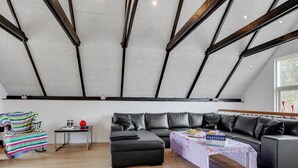 A modern loft with exposed wooden beams, a black leather sofa, a colorful striped chair, and a small table with a book and a red vase.