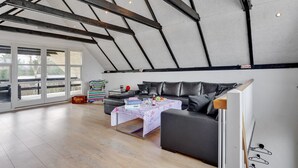 A spacious loft with a high ceiling, exposed beams, a large window, and a cozy seating area with a table.