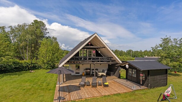 A modern house with a large deck, a covered outdoor seating area, and a small cabin-like structure.