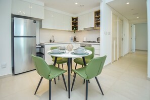 Eine moderne Küche mit weißen Schränken, einem Edelstahlkühlschrank und einem Essbereich mit rundem Tisch und grünen Stühlen.