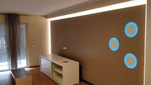 A modern living room with a built-in entertainment unit, a large window with blinds, and a wall with circular light fixtures. - Modern and spacious apartment between sea and mountain (Val Vomano)