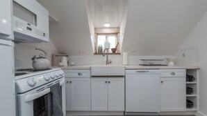 A compact kitchen with white cabinetry, a stove, a sink, and a window above the sink.